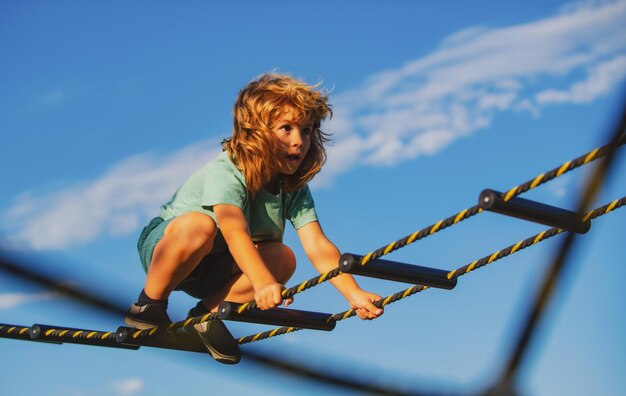 Leuke jongen klimt de ladder op de speelplaats op Kind klimt de ladder op tegen de blauwe lucht youn