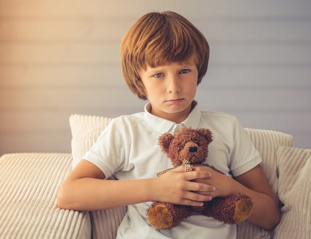 Leuke jongen knuffelt een teddybeer en kijkt naar de camera.