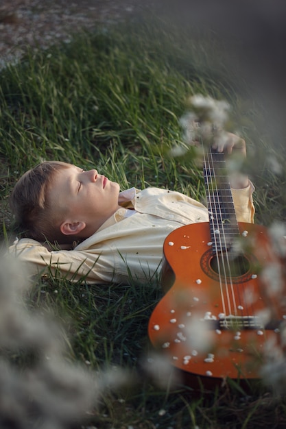 Leuke jongen ligt op het gras met een gitaar op zonsondergang