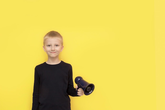 Leuke jongen met een megafoon in zijn hand op een gele achtergrond met kopieerruimte