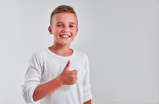 Foto leuke jongen op een grijze achtergrond stak zijn vinger op en zegt ok en glimlacht.