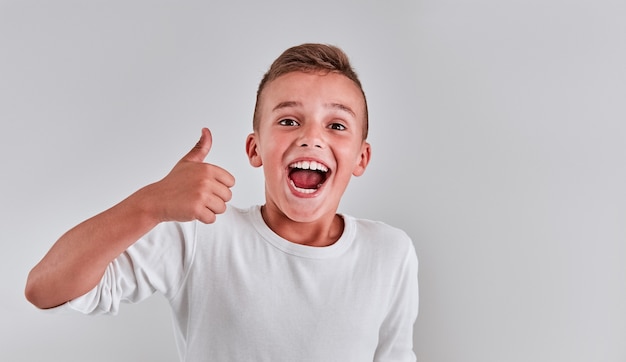 Foto leuke jongen op een grijze achtergrond stak zijn vinger op en zegt ok en glimlacht.