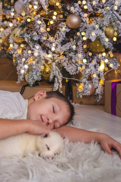 Leuke jongen slapen met een puppy onder de kerstboom in de lichten van de slinger, Nieuwjaar