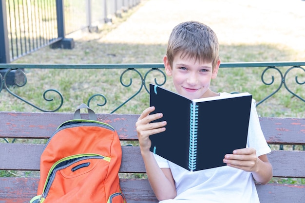 Leuke jongensstudent die een boeknotitieboekje leest zittend op een bankje op straat Voorbereiding op een lezing op school