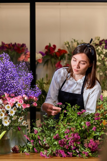 Leuke kaukasische bloemist die boeket maakt, ervaren dame die bloemen schikt