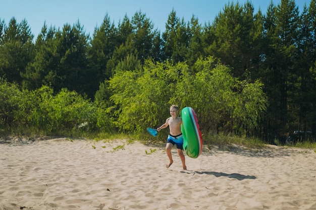 Leuke kaukasische jongen met rubberen ring en vlindernet die lachend in het water loopt Vakantie aan zee Gelukkige jeugd Afbeelding met selectieve focus