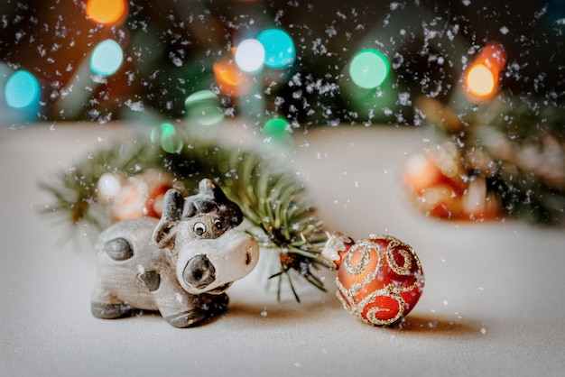 Leuke keramische stier als symbool van nieuwjaar 2021 op wazig bokeh achtergrond naast tak van de kerstboom versierd met rode bal