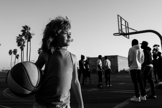 Leuke kindjongen speelt basketbal. Actieve kinderen genieten van buitenspel met basketbalbal op het basketbalveld van Venice Beach.