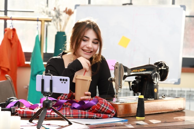 Leuke kleermaker die een koffiekopje vasthoudt en naar haar telefoon glimlacht