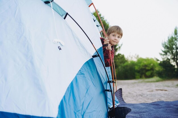 Leuke kleine blanke jongen die uitkijkt vanuit een toeristische tent Familie camping concept