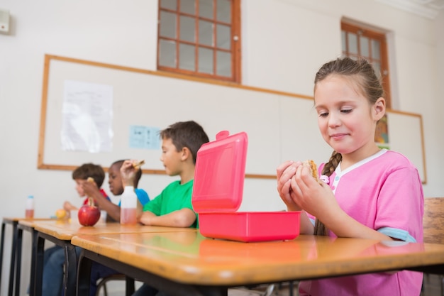 Leuke leerling die lunchbox opent bij bureau in klaslokaal