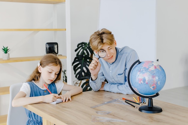 Leuke leerlingen kijken naar globe in de klas op de school Jongen die vergrootglas vasthoudt en naar de camera kijkt Conceptie van onderwijs