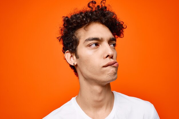 Leuke man in wit T-shirt krullend haar grimace oranje achtergrond foto van hoge kwaliteit