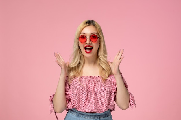 Leuke meid, mooie blonde dame met een rode bril in een roze shirt die opwindend met de handen zwaait