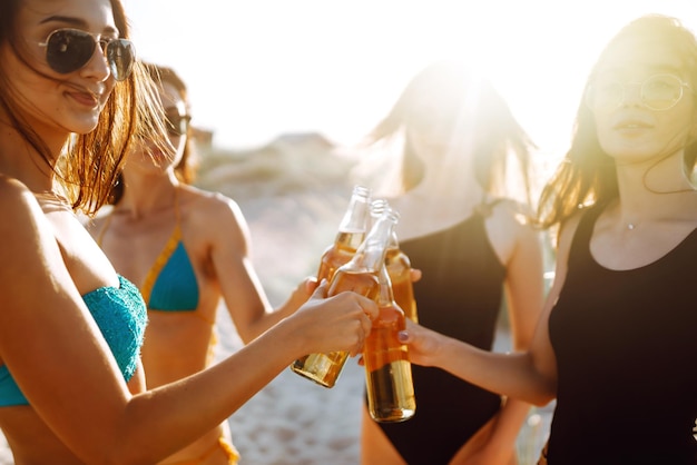 Leuke meisjes juichen en drinken bier op het strand bij zonsondergang vier meisje in bikini genieten op het strand vakantie