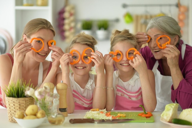 Leuke meisjes met moeder en grootmoeder die heerlijke verse salade in keuken bereiden