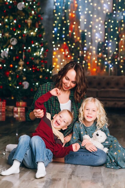 Leuke moeder met dochter en zoon poseren bij de kerstboom