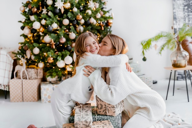 Leuke moeder met dochter knuffelen in de buurt van kerstcadeaus naast de kerstboom