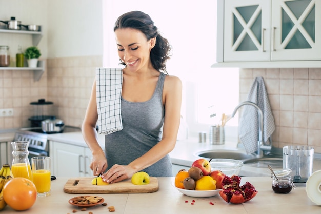 Leuke mooie en gelukkige jonge brunette vrouw in de keuken thuis is appels hakken