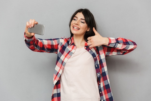 Leuke mooie jonge dame maken selfie door mobiele telefoon duimen opdagen.