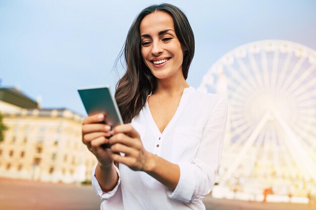 Leuke mooie jonge gelukkige vrouw die smartphone op stadsachtergrond gebruikt