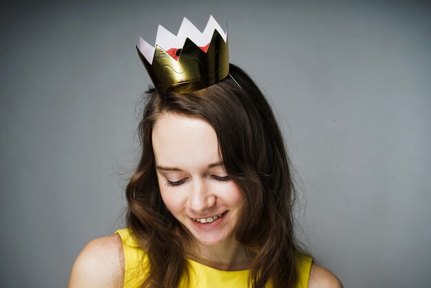 Foto leuke mooie jonge vrouw in een gele jurk glimlachend, op haar hoofd een gouden kroon