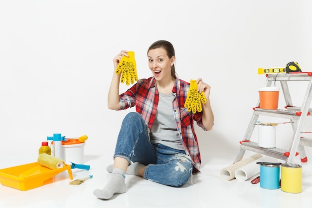 Leuke mooie vrouw in casual kleding zittend op de vloer met gele handschoenen, instrumenten voor renovatie appartement geïsoleerd op een witte achtergrond. Behangaccessoires voor tekengereedschappen. Reparatie thuis concept