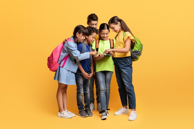 Leuke multi-etnische scholierenkinderen die digitale tablet op geel bekijken