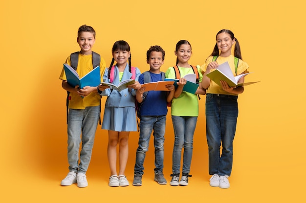 Leuke multi-etnische schoolkinderen met rugzakken met schoolboeken gele achtergrond