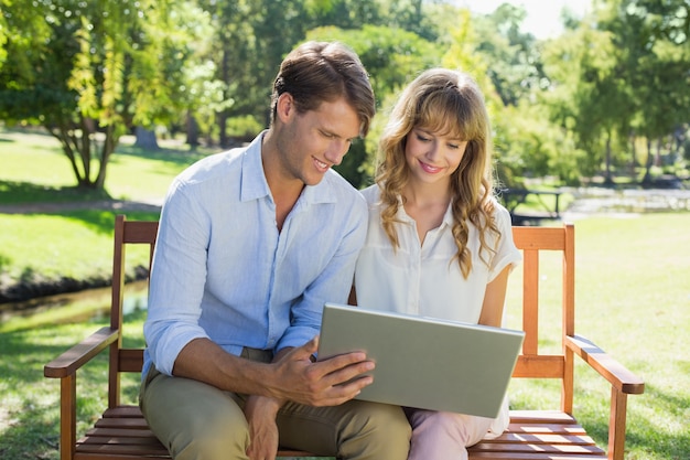 Leuke paarzitting op parkbank die samen laptop bekijkt