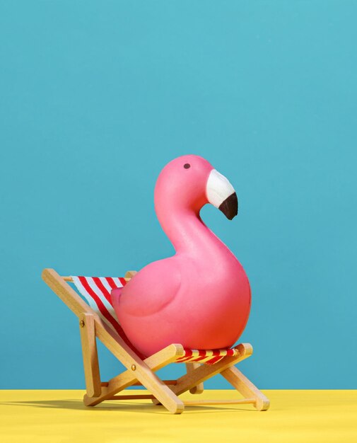 Foto leuke roze flamingo zit op een strandstoel op een blauwe en gele achtergrond.