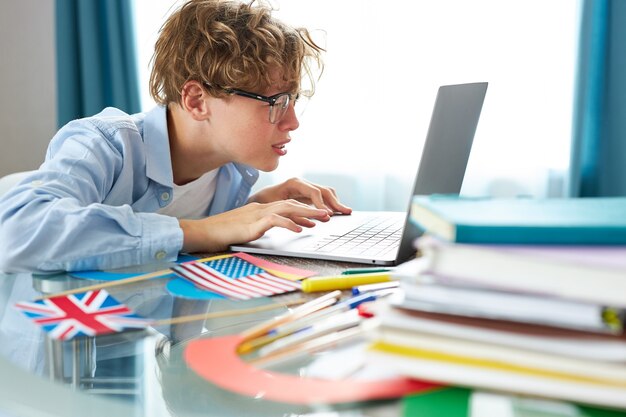 Leuke schooljongen zegt hallo tegen de camera terwijl ze thuis online les heeft