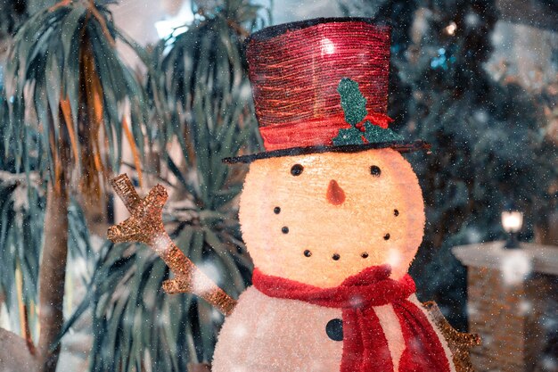 Leuke sneeuwpop met muts en sjaal in sneeuwval versieren in achtertuin op kerstfestival