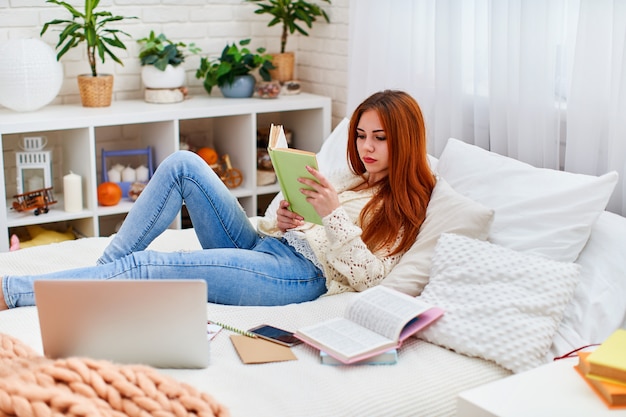 Leuke studentenvrouw die thuiswerk doet dat op het bed thuis ligt