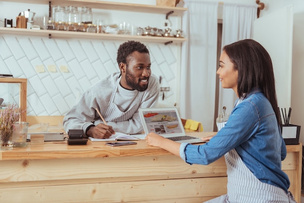 Leuke suggesties. Vrij vrouwelijke barista zit aan de balie van het café voor haar collega en bespreekt met hem het ontwerp van hun website terwijl de man aantekeningen maakt