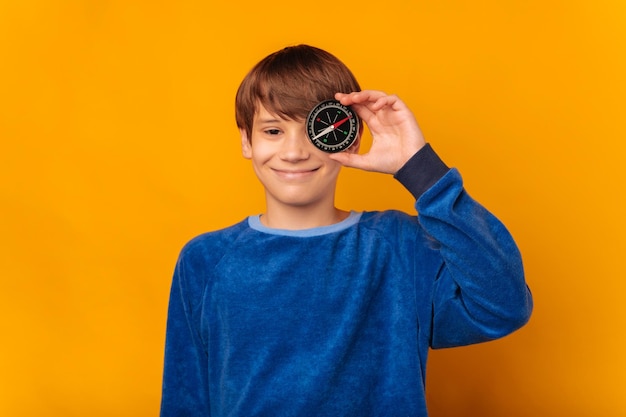 Leuke tienerjongen die blauw draagt, houdt een kompas van het leven voor een oog