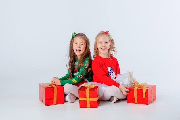 Leuke twee kleine meisjes in rode trui, geschenkdoos zitten witte achtergrond Kerstmis concept tekstruimte