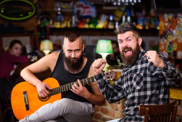 Leuke vrienden zingen liedjes gitaarmuziek ontspanning in de pub vrienden ontspannen in de pub live muziek concert man speelt gitaar in de pub akoestische optreden in de pub hipster bruut baard met vriend in de pub