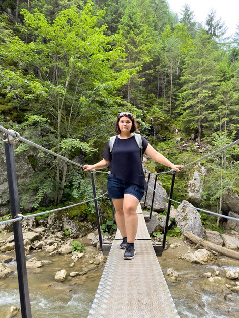 Leuke vrouw die een hangbrug over een rivier in het bos oversteekt.