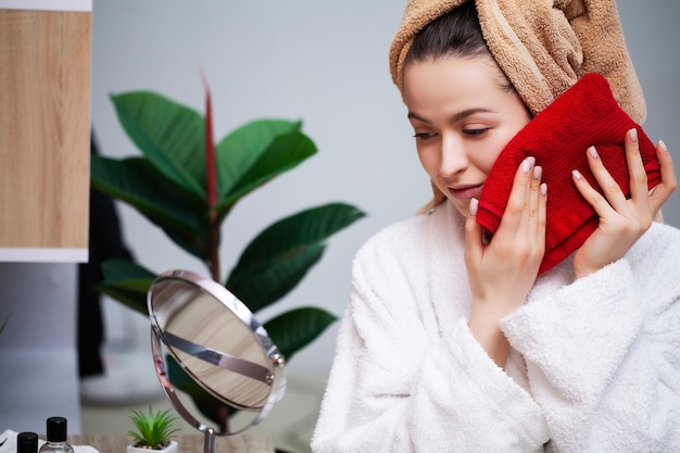 Leuke vrouw in de badkamer veegt haar gezicht af na een douche met een badstof handdoek