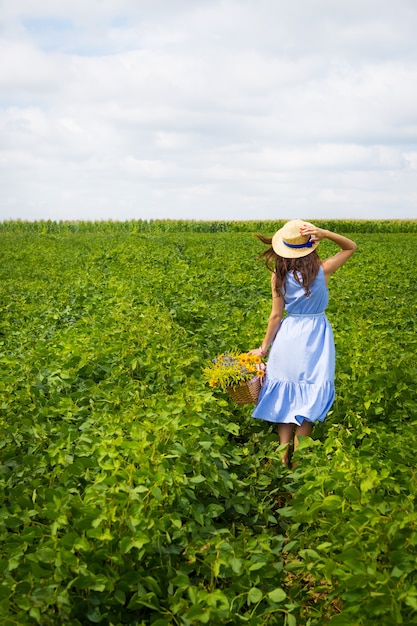 Leuke vrouw in een hoed staat in een groen veld met een boeket wilde bloemen