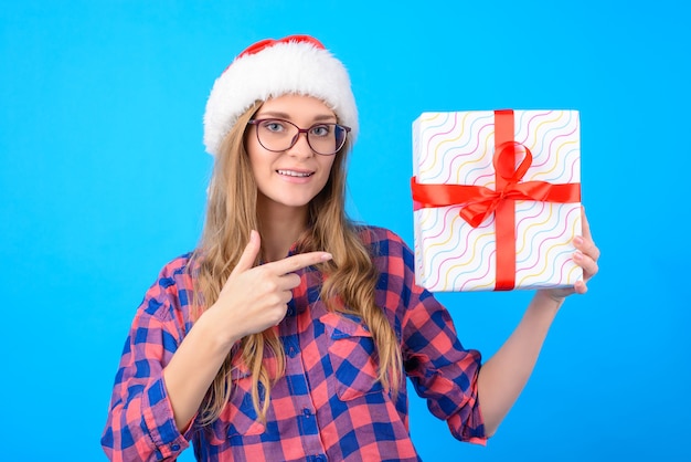 Leuke vrouw in glazen en kerstmuts wijzend op de geschenkdoos in haar hand