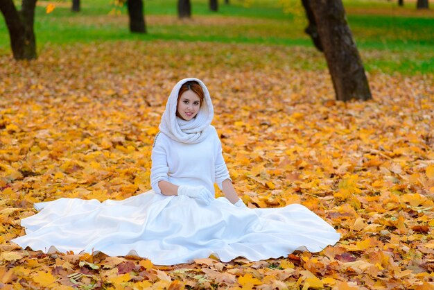 Leuke vrouw in lange witte trouwjurk onder herfstbomen