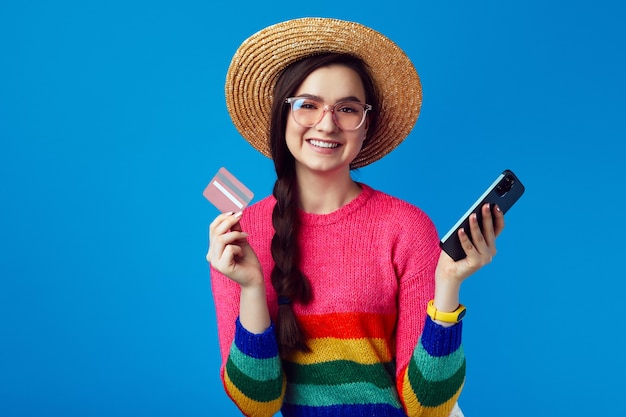 Leuke vrouw in regenboogtrui met plastic creditcard en smartphone