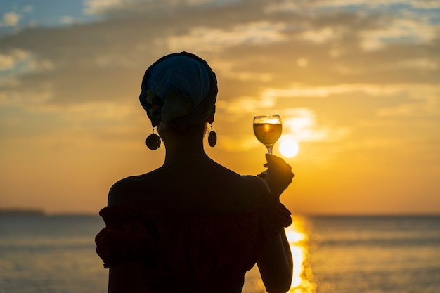 Foto leuke vrouw met glas witte wijn tegen een prachtige zonsondergang in de buurt van zee golven op het tropische strand, close-up. meisje geniet van de zonsondergang met een glas wijn. concept van vrije tijd en reizen