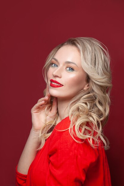 Foto leuke vrouw met make-up en blond krullend haar glimlachend op rode achtergrond