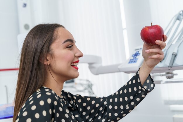 Leuke vrouw met rode lippen. Patiënt op het kantoor van de tandarts. Vrouw met appel.