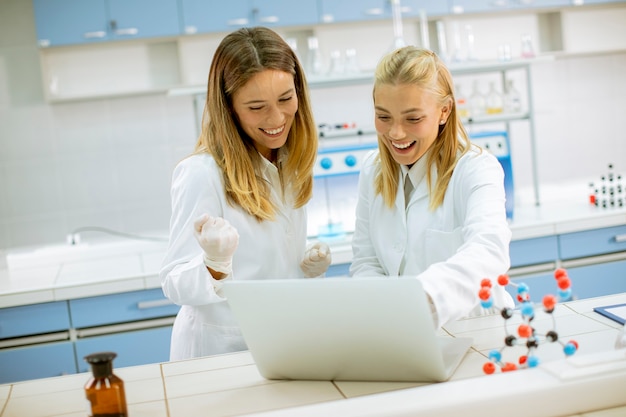 Leuke vrouwelijke onderzoekers in witte laboratoriumjas met behulp van laptop tijdens het werken in het laboratorium