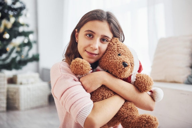 Leuke vrouwelijke tiener binnenshuis in de woonkamer op vakantietijd met teddybeer.