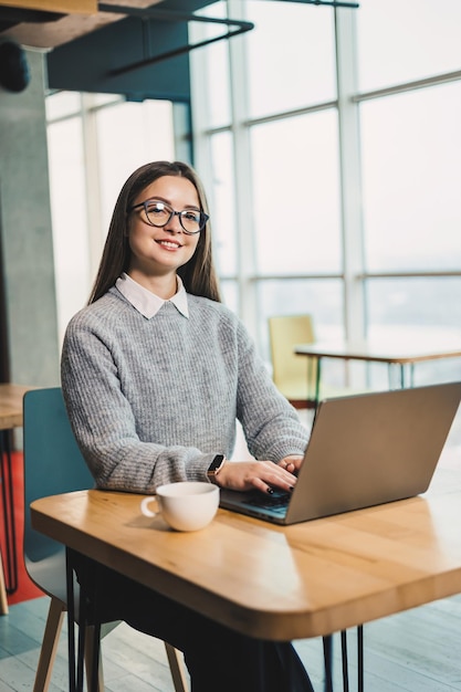 Leuke zakenvrouw zit aan een bureau in een moderne werkruimte en werkt aan een laptop Werkproces van een vrouw in het kantoor